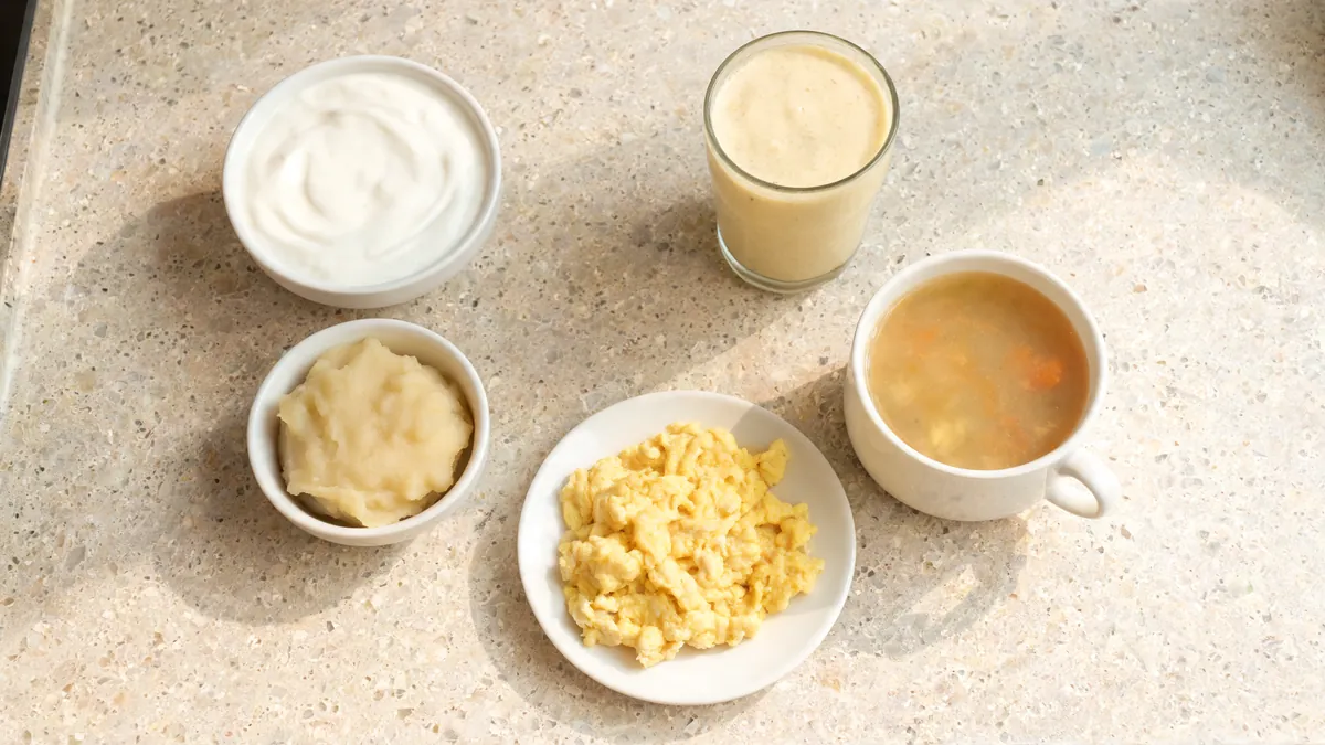 Soft foods on a kitchen counter, including yogurt, mashed potatoes, soup, scrambled eggs and a smoothie